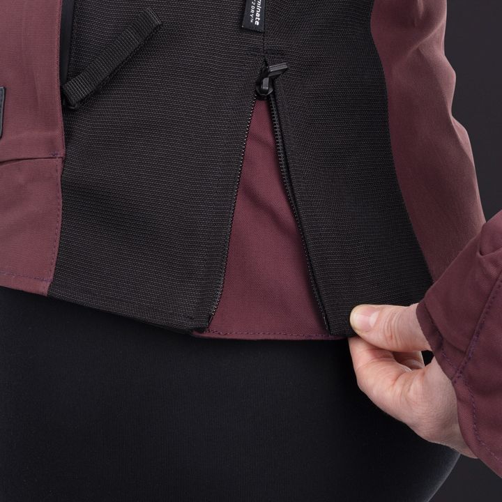 Close-up of a person's torso with a hand partially opening a black zipper on a burgundy and black garment.