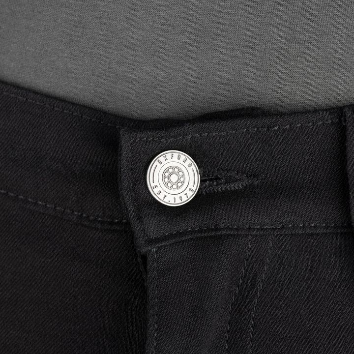 Close-up of a silver button on black denim jeans with the button featuring engraved text and design.