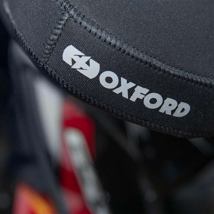 Close-up of a black Oxford branded motorcycle accessory with focus on the logo, hint of a motorcycle in the background.