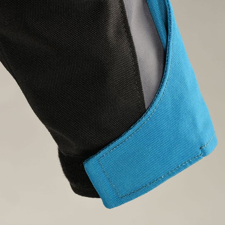 Close-up of a jacket sleeve with black fabric and a blue cuff with Velcro fastening on a gray background.