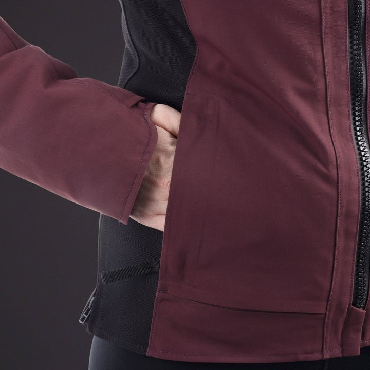 A close-up of a person wearing a burgundy jacket with their hand tucked in the pocket, over a black garment with a visible zipper.