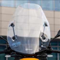 Piaggio 1 Tall Windshield Kit E5 Close-up of a motorcycle windshield with blurred building in the background.