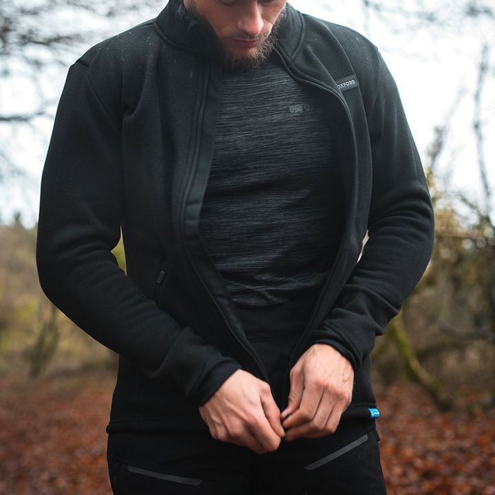 A man in sportswear zipping up a black jacket with a forest background.