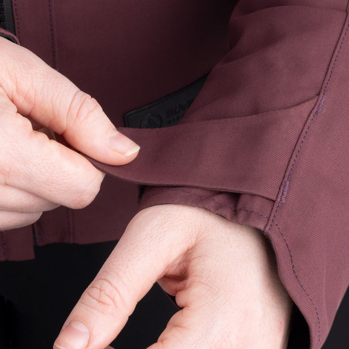 A person is taking money out of a wallet inside a hidden pocket of a burgundy jacket.