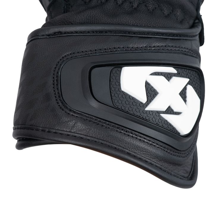 A close-up of a black motorcycle glove with a white and black knuckle protector featuring a letter "X" logo.