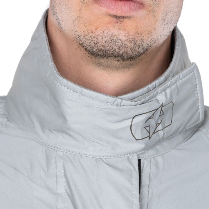 Close-up of a man's lower face and neck showing a stubbled chin with the collar of a light grey jacket featuring a logo on the right side.