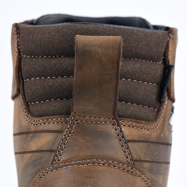 Close-up of a brown leather boot showing detailed stitching and texture against a white background.