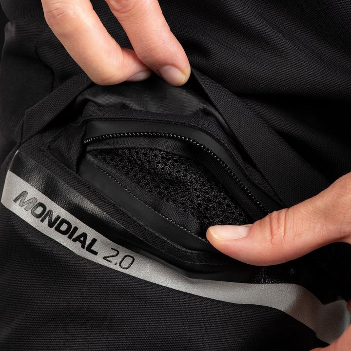 Close-up of a hand opening a black zipper pocket on a garment with the text "MONDIAL 2.0" on the interior label.