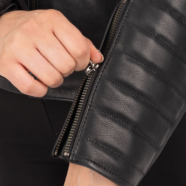 A close-up of a person's hand zipping up a black leather jacket.