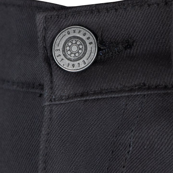 Close-up of a metal button on black fabric with engraved text and a design, possibly on a garment.