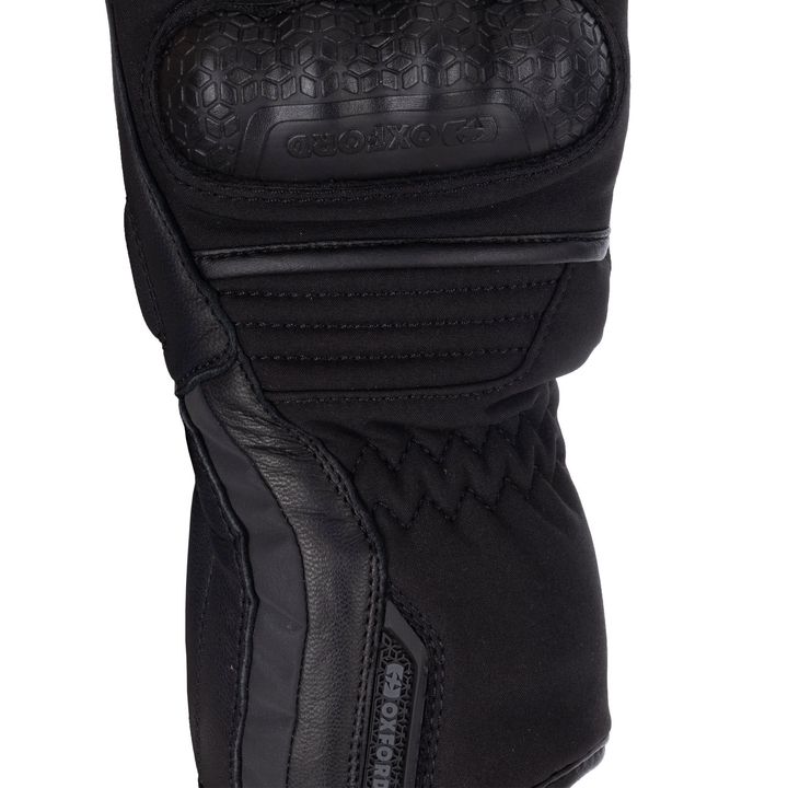 A close-up image of a black motorcycle glove, showing textured protective padding on the knuckles and multiple layers of stitched fabric for added durability.