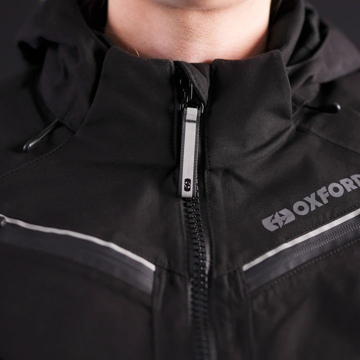 Close-up of a person wearing a black "OXFORD" jacket with a partially zipped front zipper.