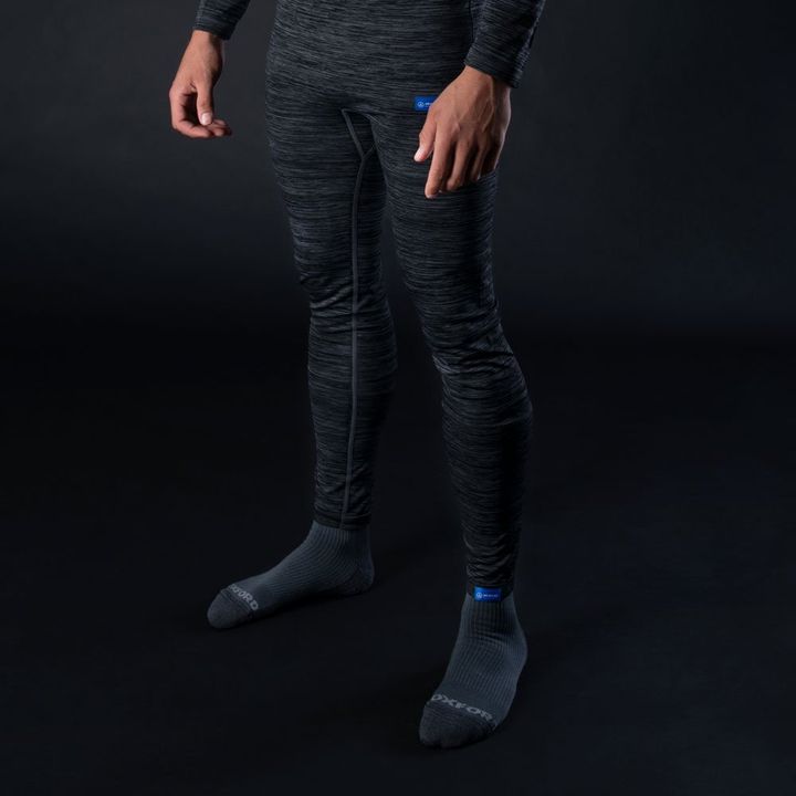 A person standing against a dark background wearing full-length grey textured athletic wear and dark grey socks.