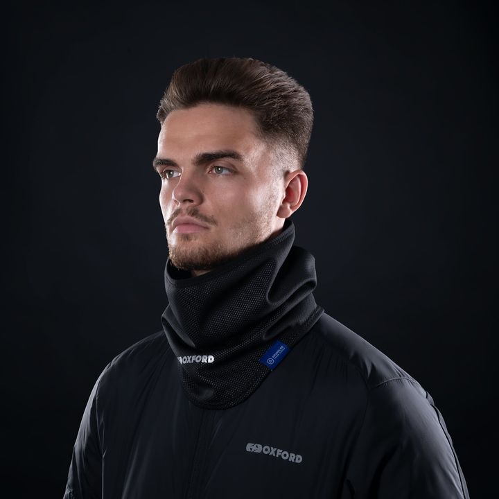 A man in profile wearing a black neck gaiter and jacket with the label 'OXFORD' on a dark background.