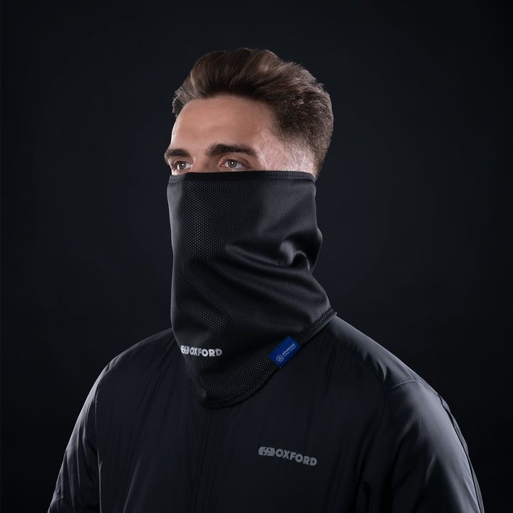 A man wearing a black balaclava and a dark jacket with the "OXFORD" logo on it against a dark background.