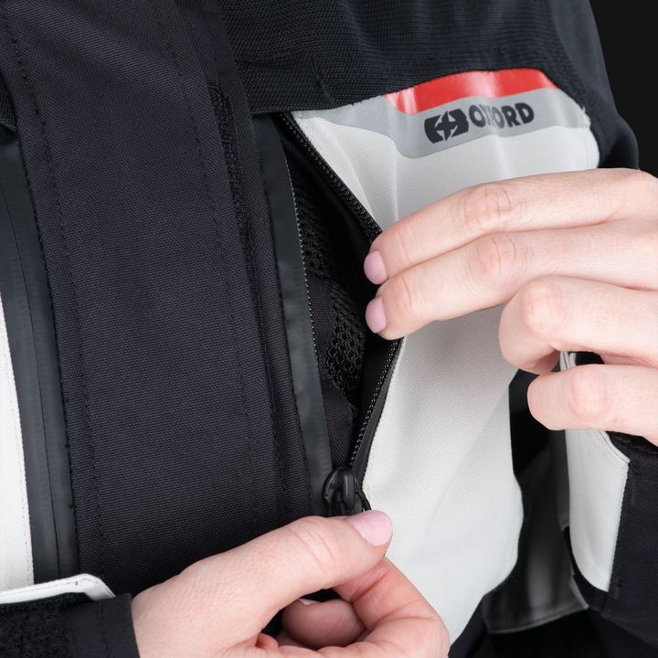 A close-up of a person's hands zipping up a black and white jacket with the "Oxford" logo visible.